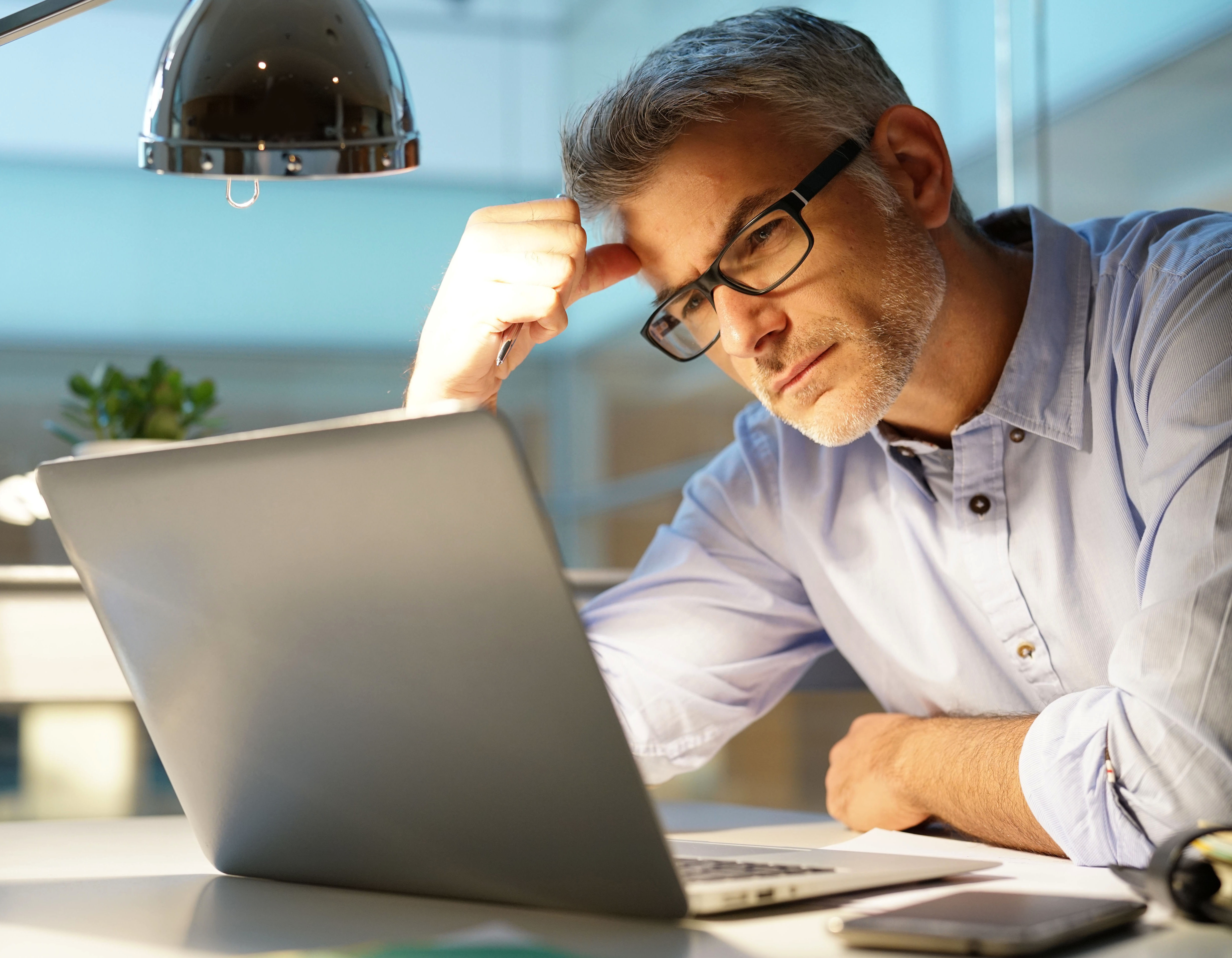 Businessman in office being thoughtful in front of laptop