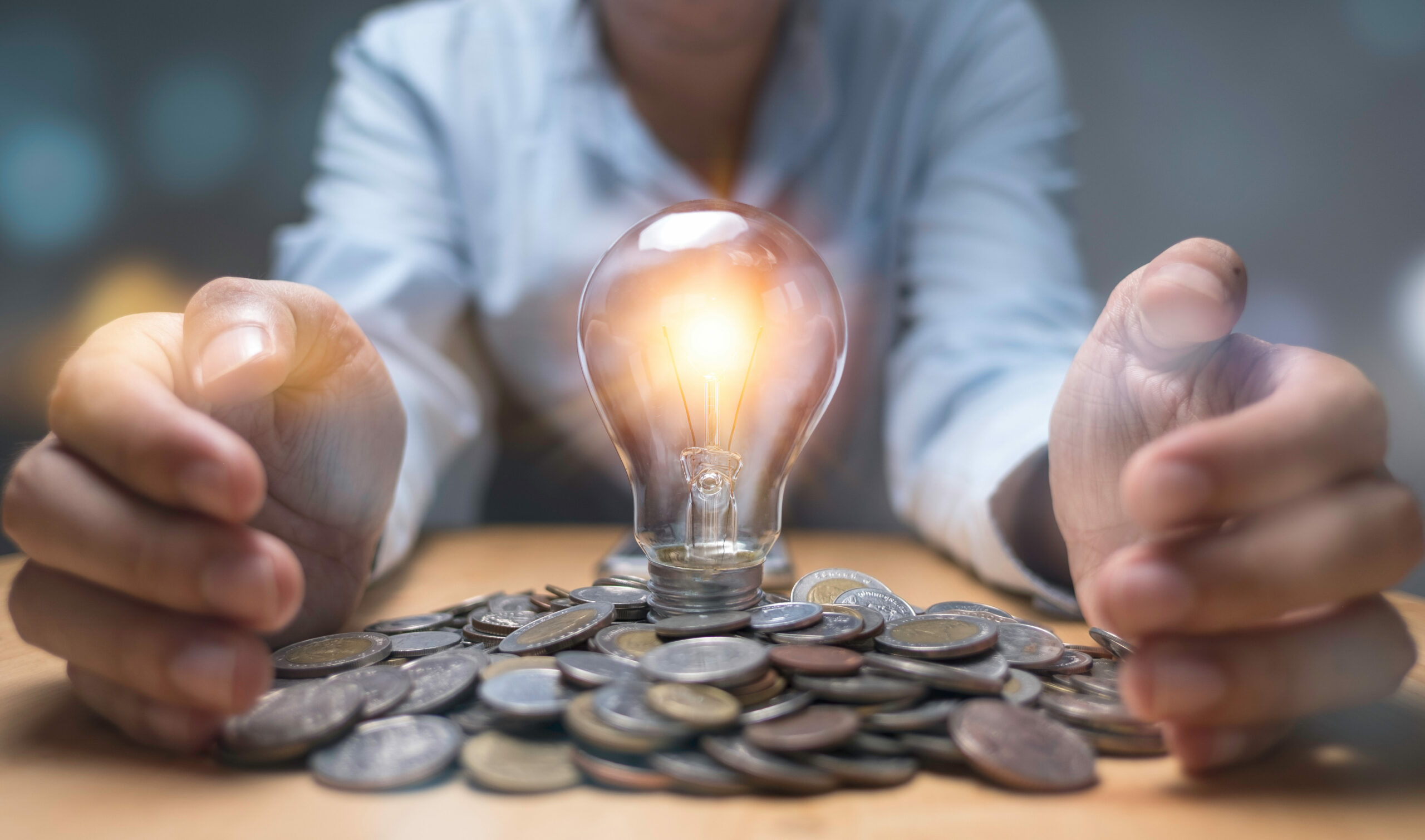 Businessman hand protecting heap of coins and lightbulb which gl