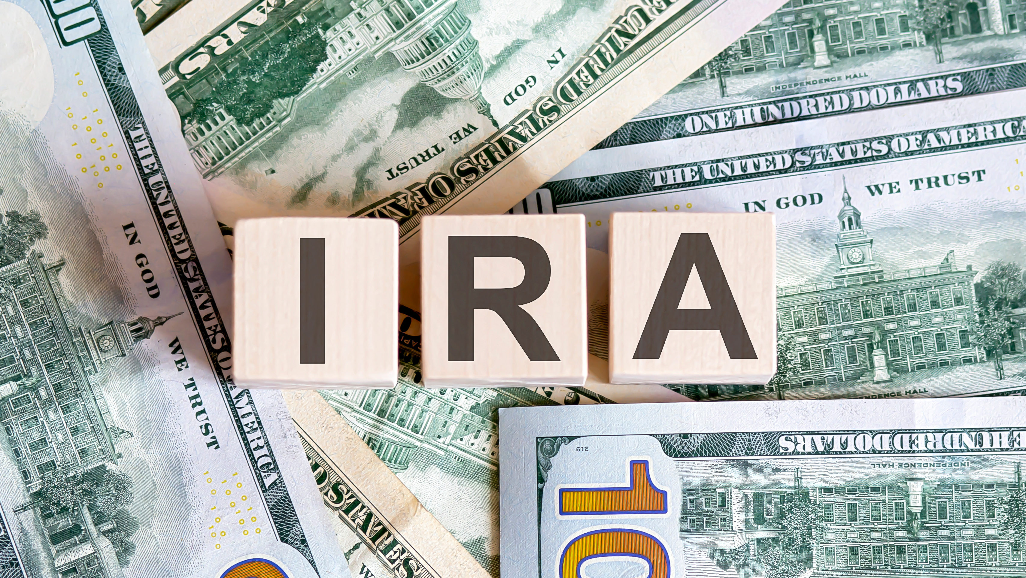 Concept words IRA on wooden blocks on a beautiful background from dollar bills.