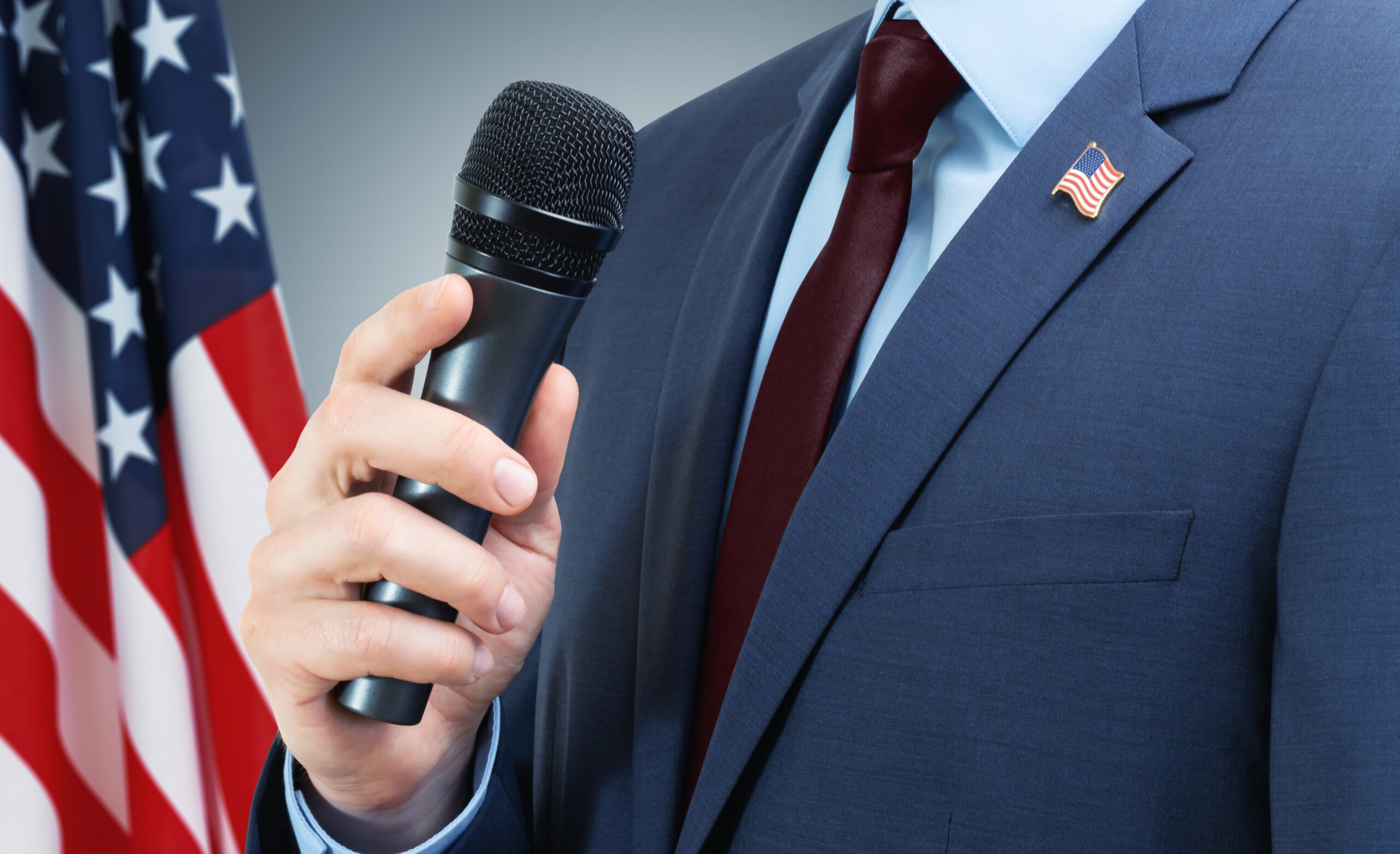 Man in suit holding microphone in hand with USA flag on backgrou